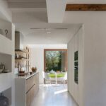 Wood and stone kitchen opening onto a dining room with a white table and a large window facing the garden