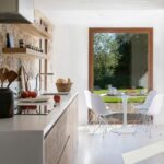 Wooden kitchen island with a white worktop and a round table with white chairs facing the large window
