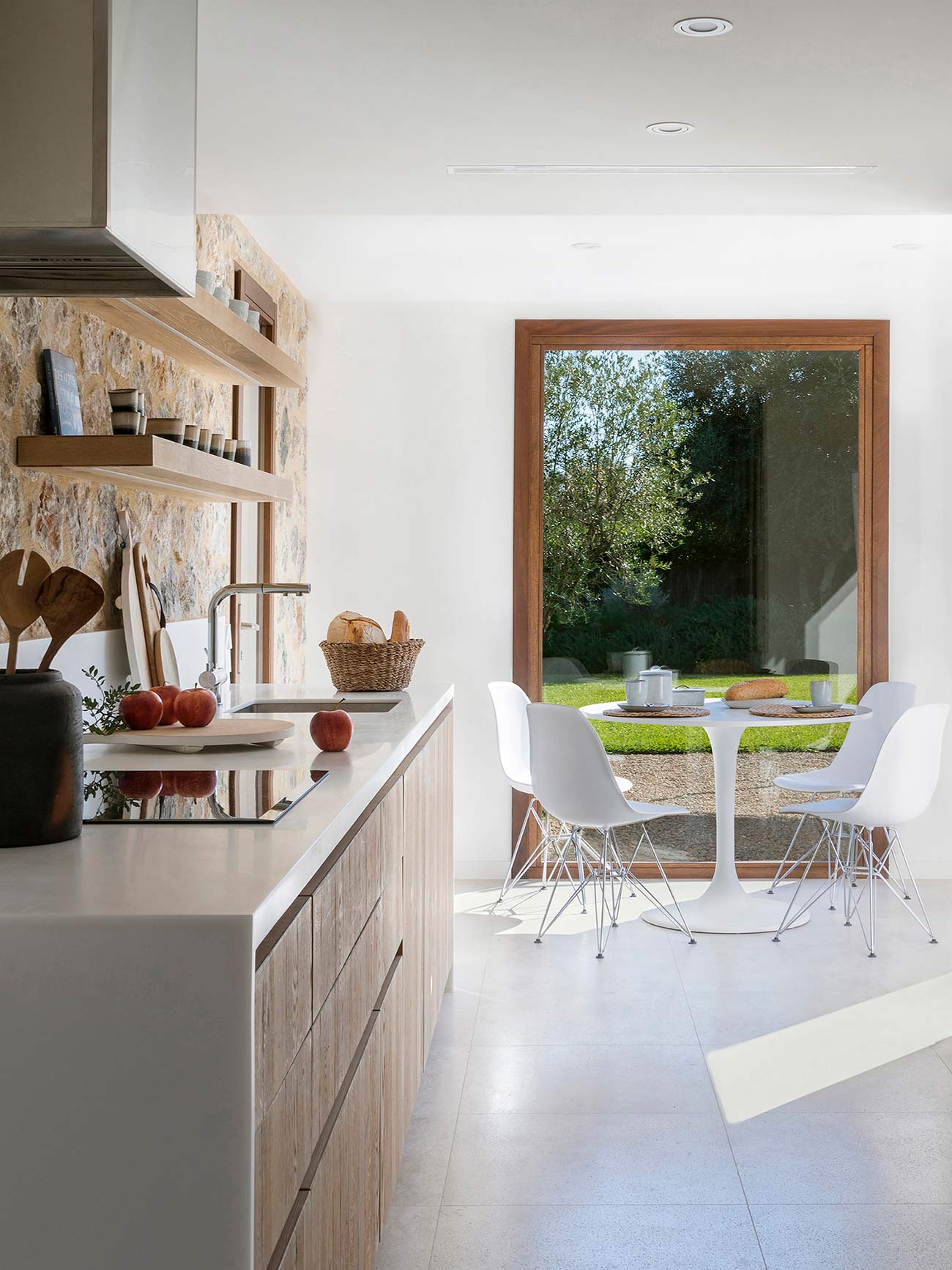 Wooden kitchen island with a white worktop and a round table with white chairs facing the large window