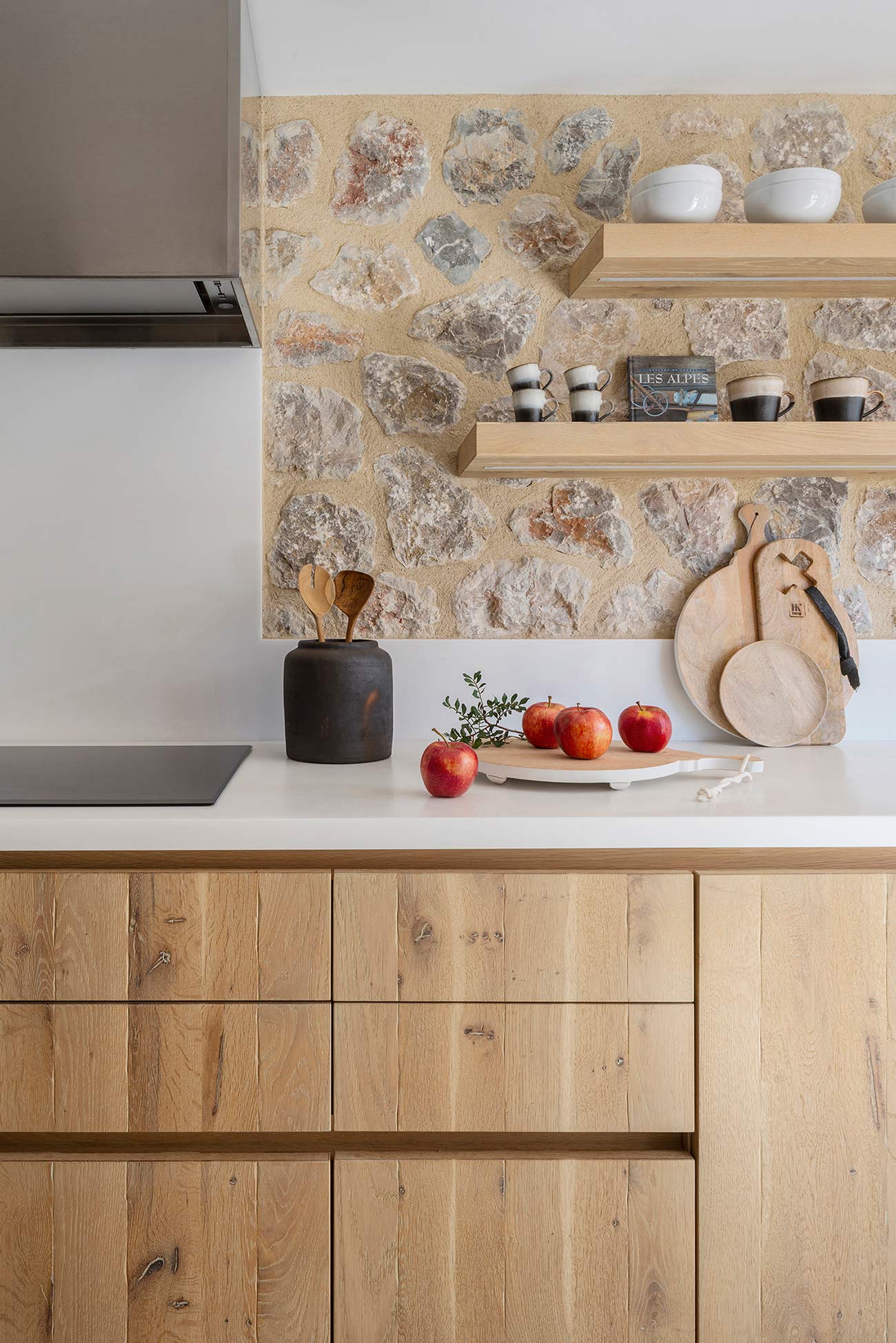 Detalle de cocina con pared de piedra, baldas y armarios de madera clara y encimera blanca