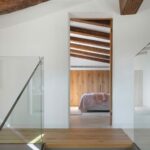 Wooden staircase with a glass balustrade leading to a bedroom with exposed beams