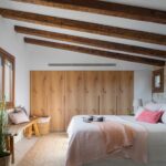 Bedroom with a sloping ceiling and timber beams, light wood wardrobes and pink bed linen