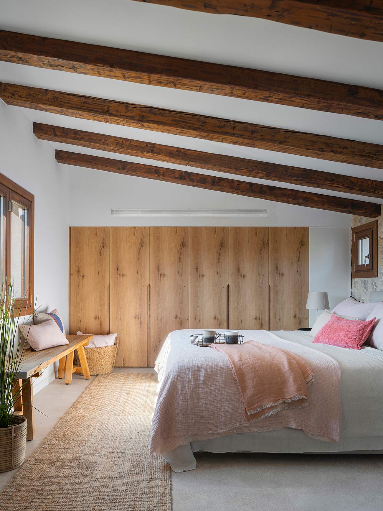 Bedroom with a sloping ceiling and timber beams, light wood wardrobes and pink bed linen