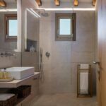 Bathroom with a glass shower, sand-coloured cladding, wooden window and exposed ceiling beams