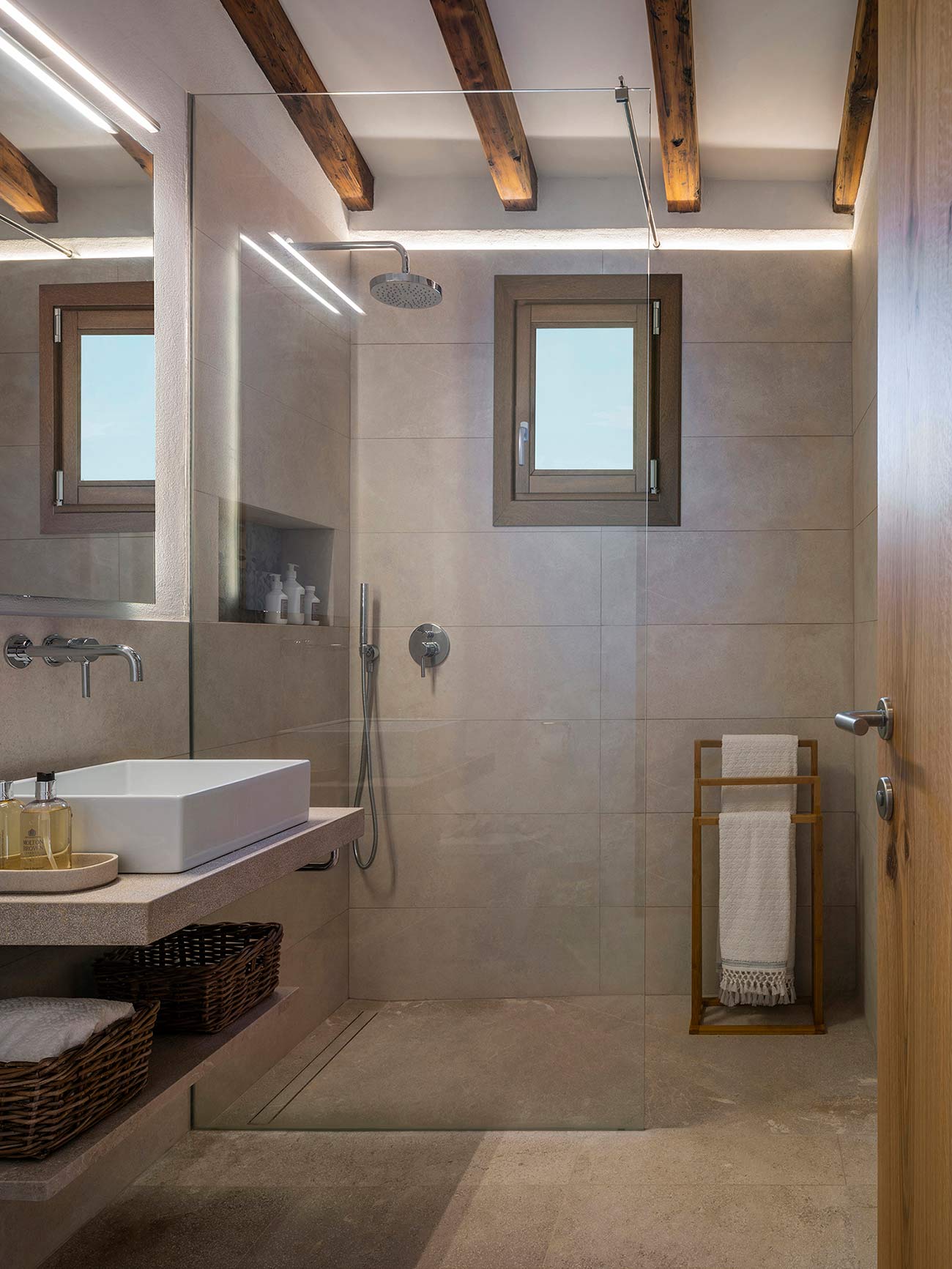 Bathroom with a white washbasin on a beige countertop, wicker baskets, wooden towel rail and wall-mounted taps