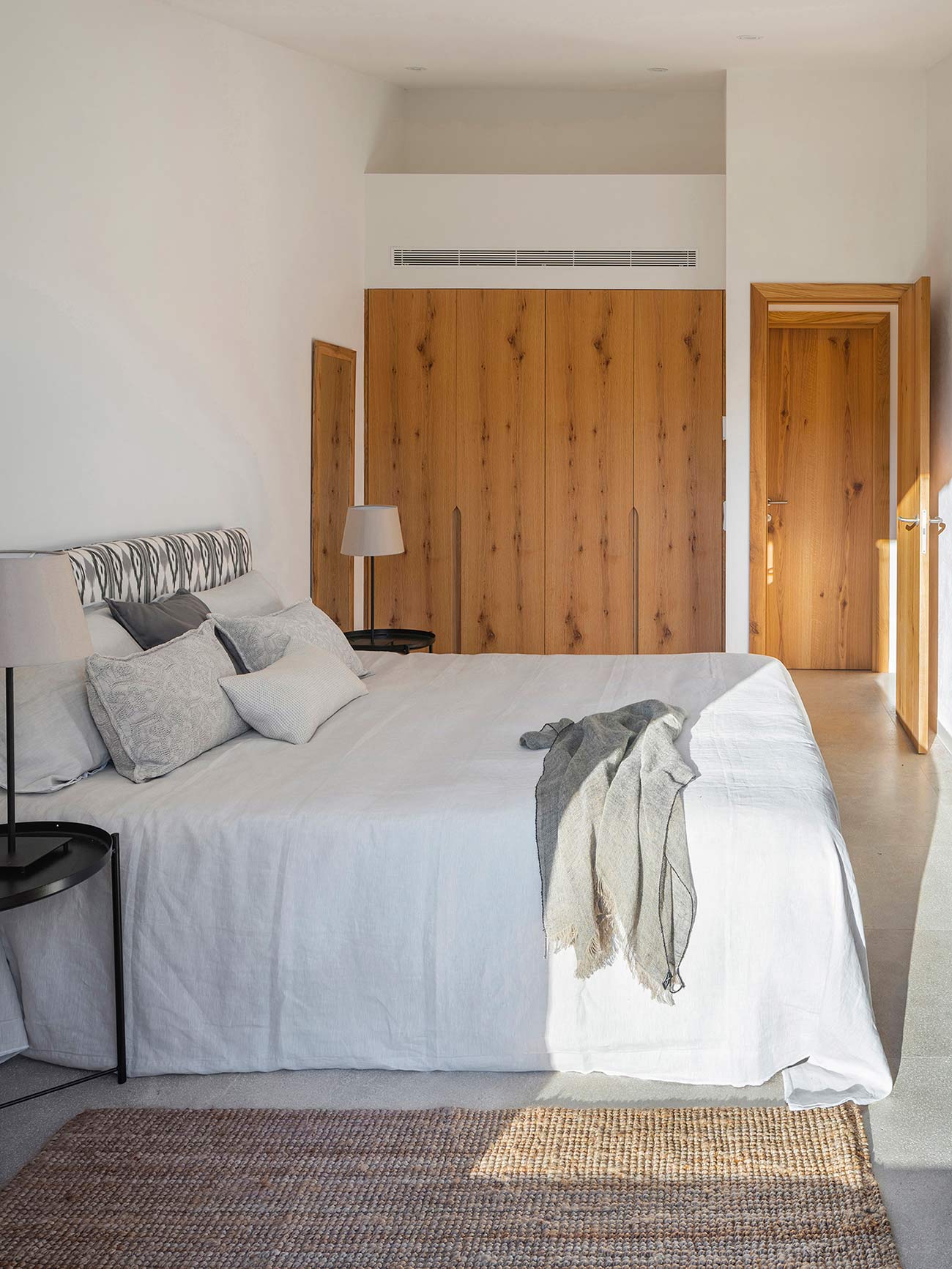 Bedroom with white bed linen, light wood wardrobes, a natural fibre rug and warm light