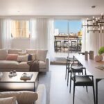 Salón y comedor abiertos con sofá claro, mesa alargada, lámpara dorada y terraza al fondo