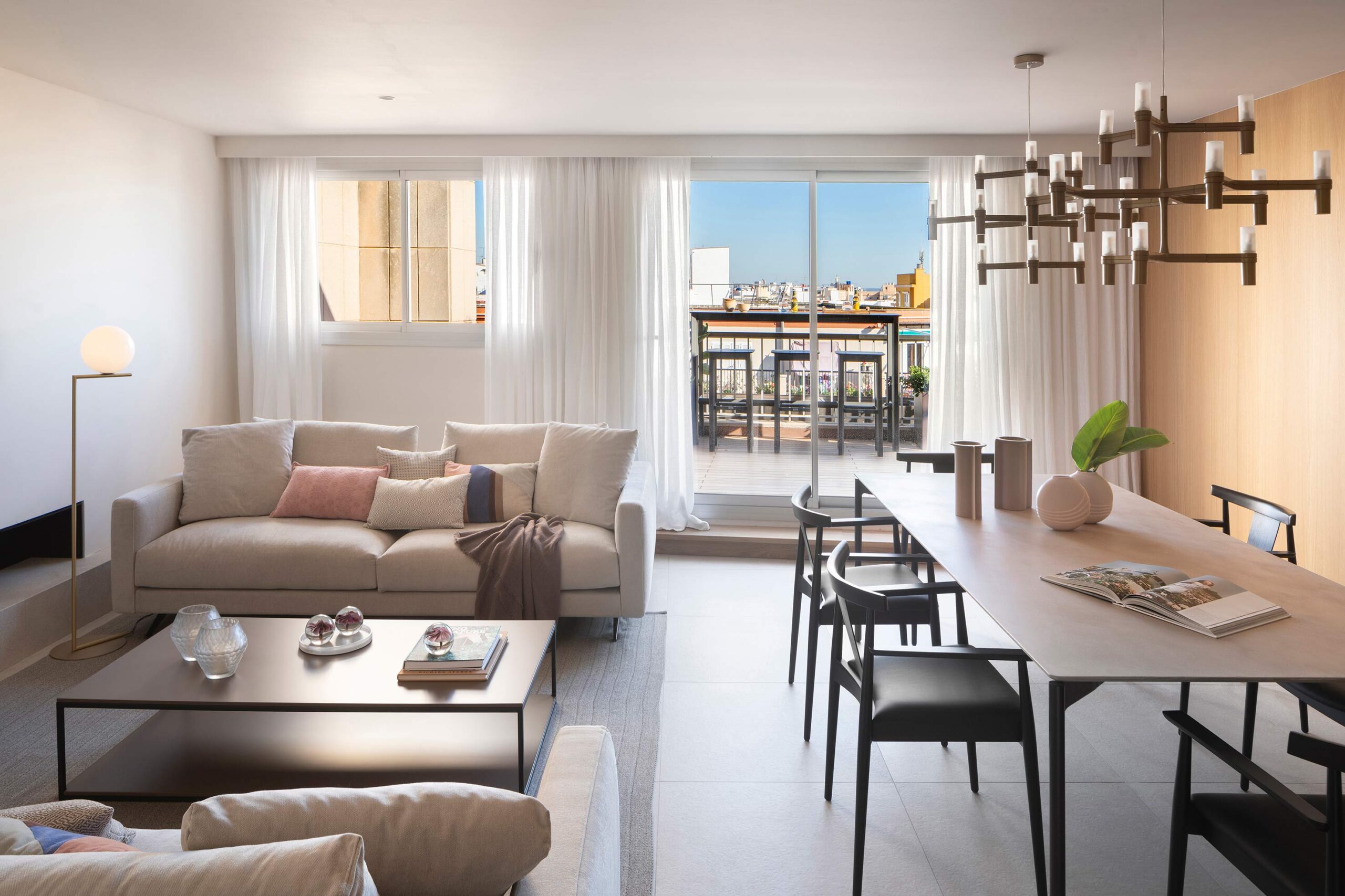 Salón y comedor abiertos con sofá claro, mesa alargada, lámpara dorada y terraza al fondo