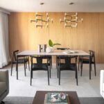 Comedor con mesa alargada, sillas negras, dos lámparas doradas y pared de madera natural junto al salón