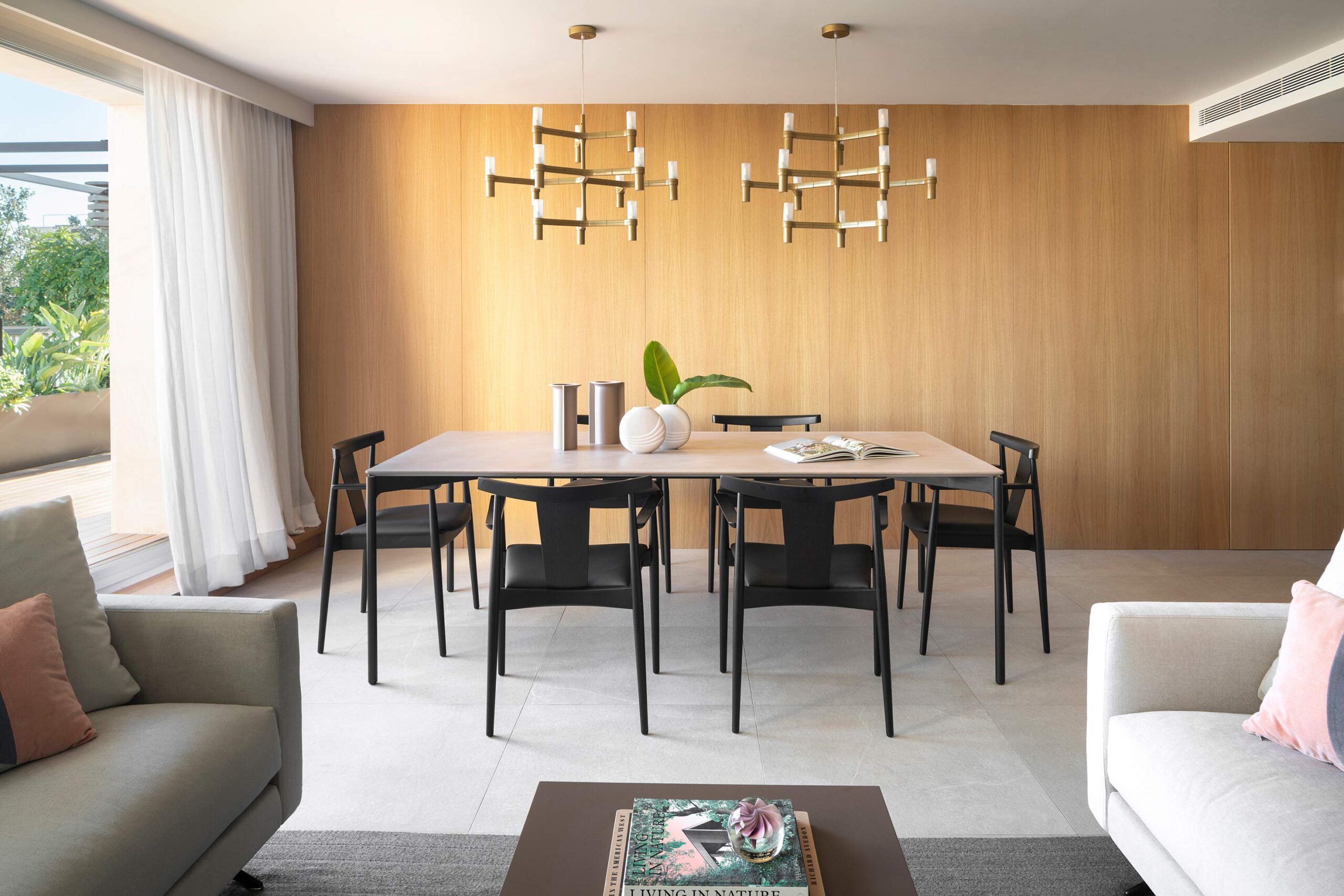 Comedor con mesa alargada, sillas negras, dos lámparas doradas y pared de madera natural junto al salón