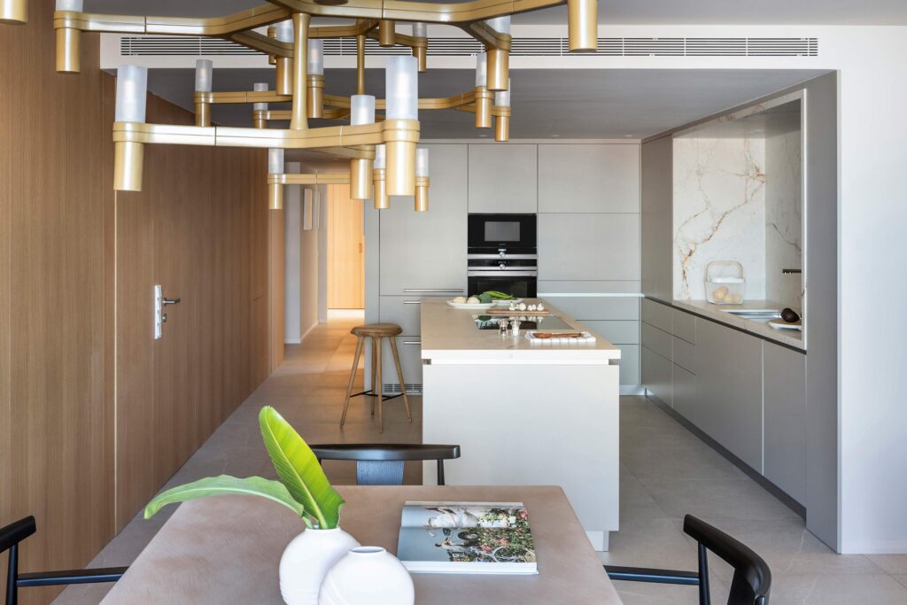 Cocina vista desde el comedor con lámpara dorada de techo, isla, panelado de madera y mesa