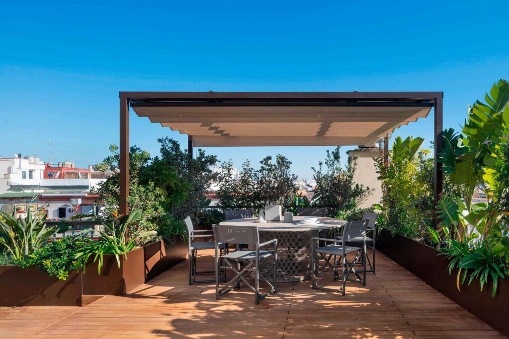 Terraza del ático Blanquerna con mesa redonda bajo pérgola de toldo retráctil y tarima de madera