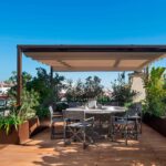 Terraza del ático Blanquerna con mesa redonda bajo pérgola de toldo retráctil y tarima de madera