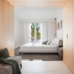 Dormitorio con cama blanca y ventanal a la terraza, visto desde un acceso con armarios de madera clara