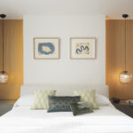 Dormitorio con cama blanca, dos lámparas colgantes de cristal, paneles de madera y cuadros azules