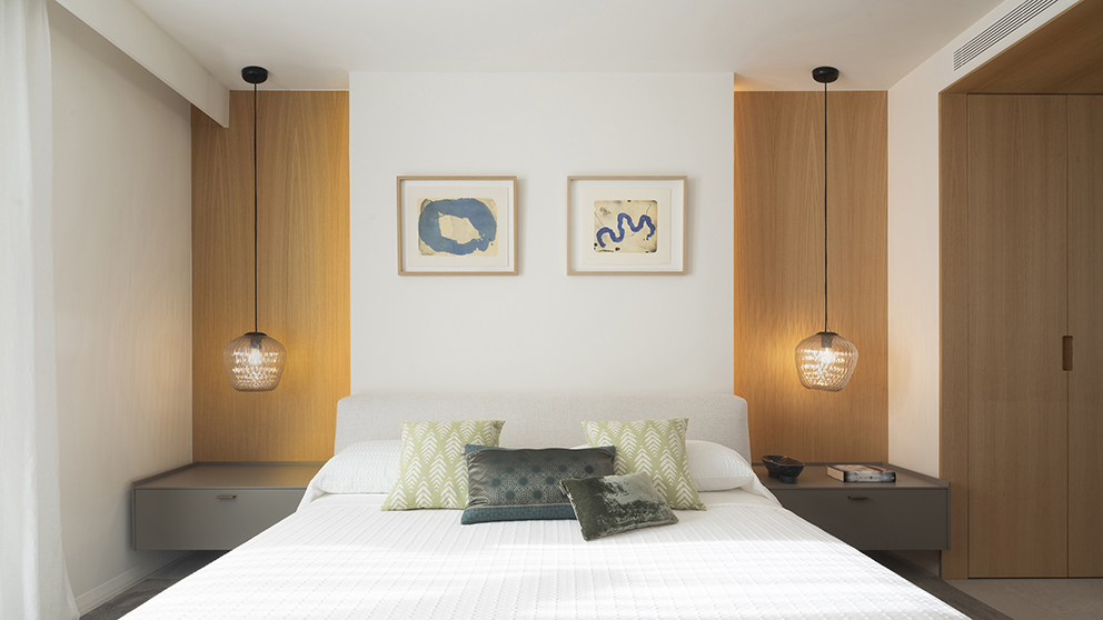 Dormitorio con cama blanca, dos lámparas colgantes de cristal, paneles de madera y cuadros azules