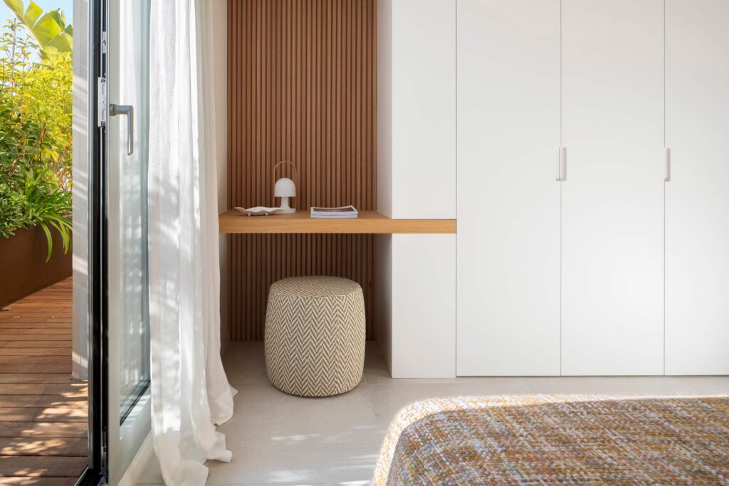 Dormitorio con escritorio de madera, panel de lamas, armario blanco y puerta acristalada a la terraza