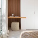 Dormitorio con escritorio de madera, panel de lamas, armario blanco y puerta acristalada a la terraza