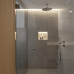 Ducha con mampara de cristal, rociador de techo, hornacina iluminada y revestimiento gris
