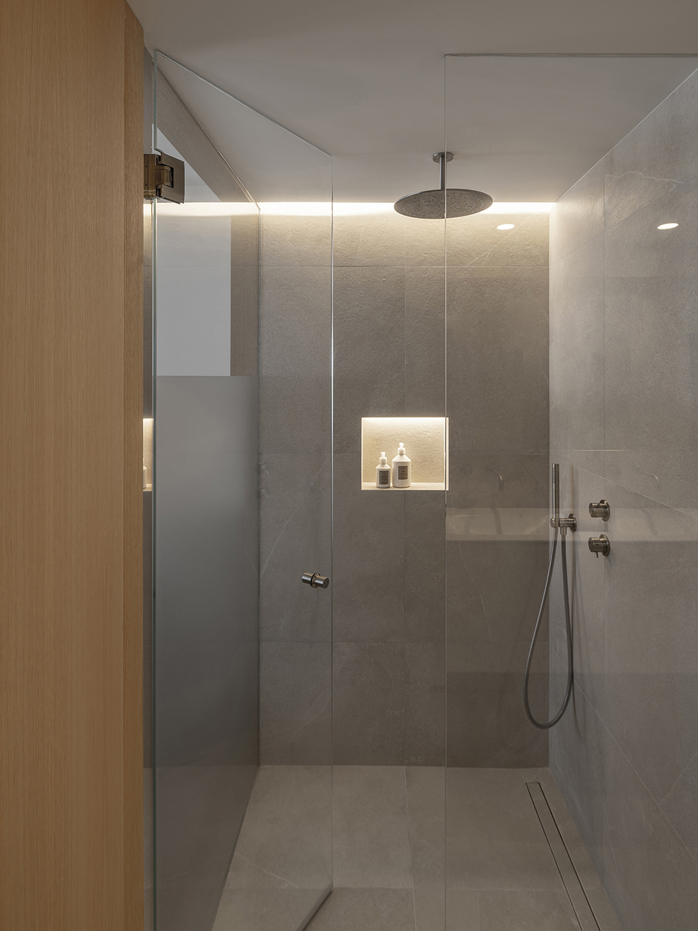 Ducha con mampara de cristal, rociador de techo, hornacina iluminada y revestimiento gris