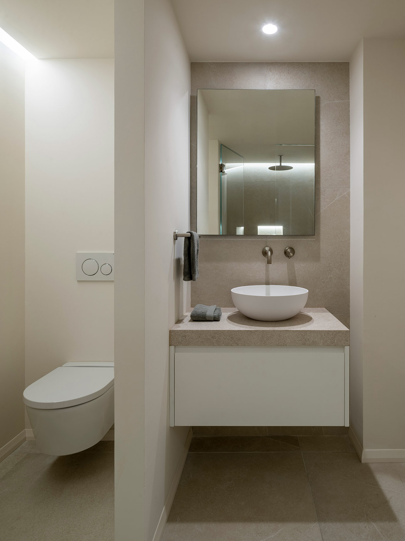 Aseo con lavabo tipo bol sobre encimera de piedra, mueble blanco suspendido, espejo e inodoro suspendido