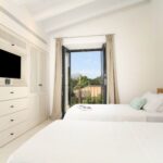 Dormitorio de dos camas con balconera abierta a la montaña, armario blanco y cojines verde agua