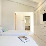 Dormitorio de camas gemelas con armario empotrado de celosía, cajonera y televisión, y baño al fondo