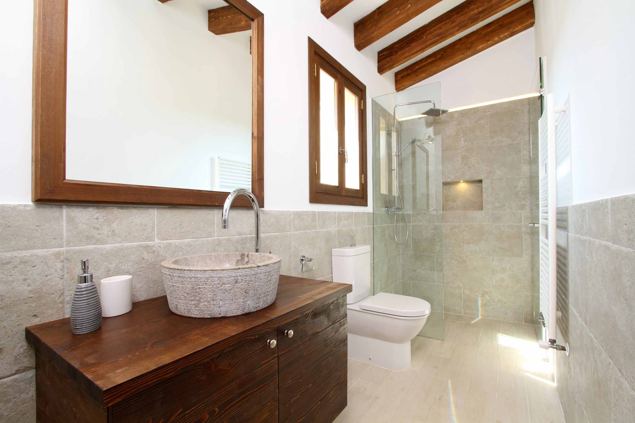 Baño con lavabo de piedra sobre mueble de madera oscura, ducha acristalada y revestimiento gris