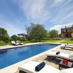 Villa Marina, piscina azul con tumbonas blancas y jardín, con la casa rústica de piedra al fondo