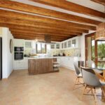 Cocina amplia con nevera de acero, mesa de cristal, vigas de madera y suelo de terracota