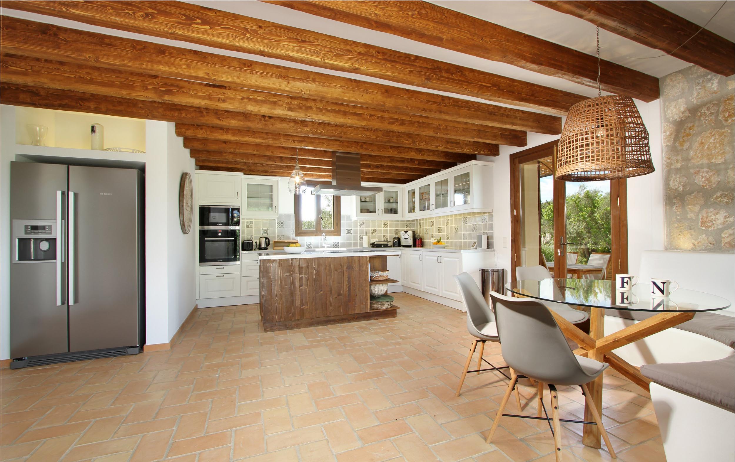 Cocina amplia con nevera de acero, mesa de cristal, vigas de madera y suelo de terracota