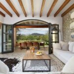 Salón con sofás blancos, pared de piedra, vigas de madera y terraza con vistas a la montaña