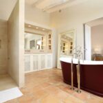 Baño con bañera exenta granate, ducha de piedra crema, suelo de terracota y mueble con celosía