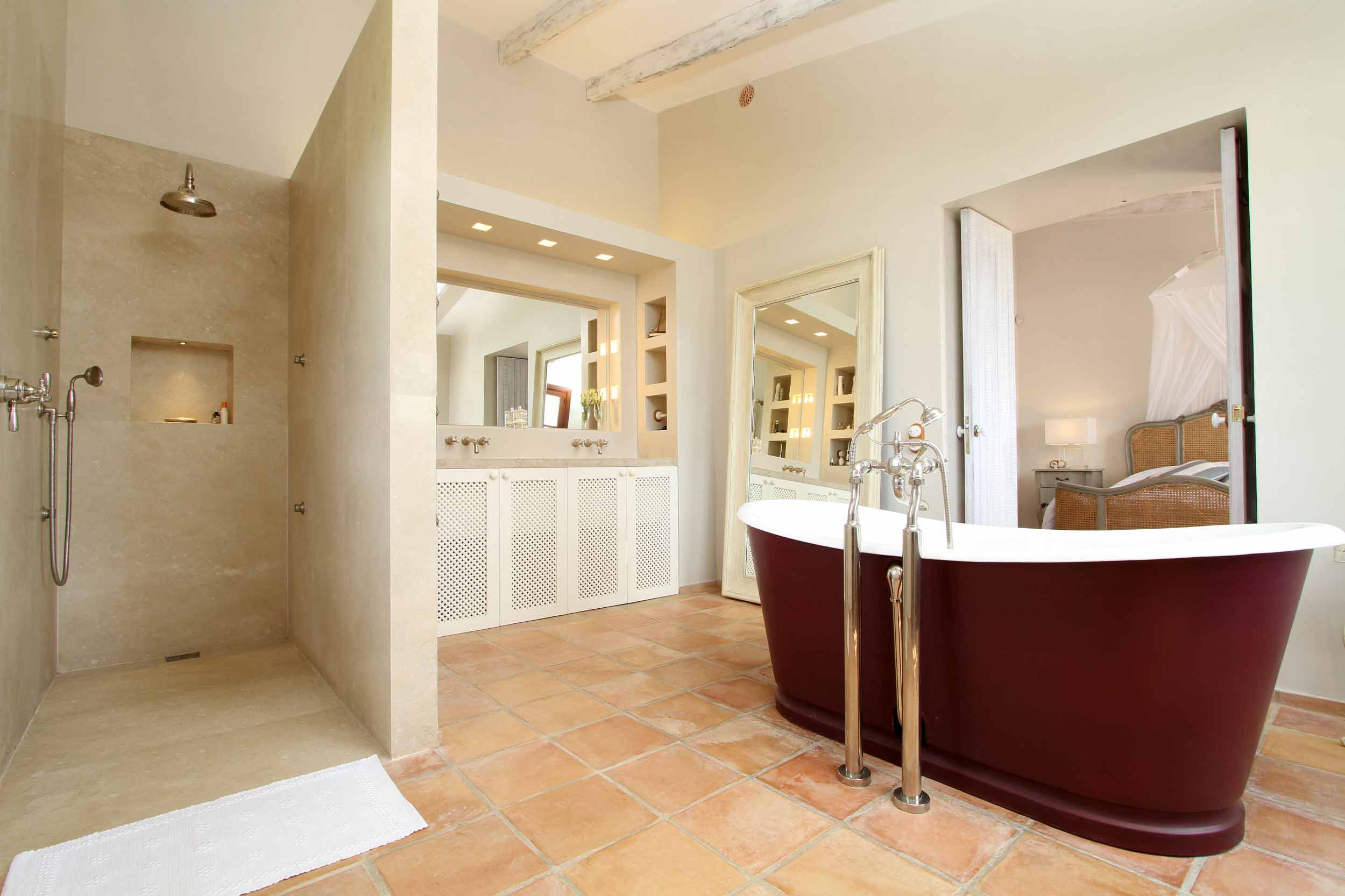 Baño con bañera exenta granate, ducha de piedra crema, suelo de terracota y mueble con celosía