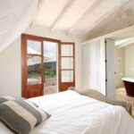 Dormitorio con dosel de gasa blanca, puerta de madera a la terraza y bañera granate al fondo