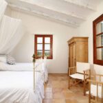 Dormitorio con dos camas de hierro, doseles blancos, ventanas de madera con vistas y suelo de terracota