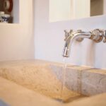 Detalle del lavabo de piedra tallada con grifo cromado de pared y cuencos azules y blancos