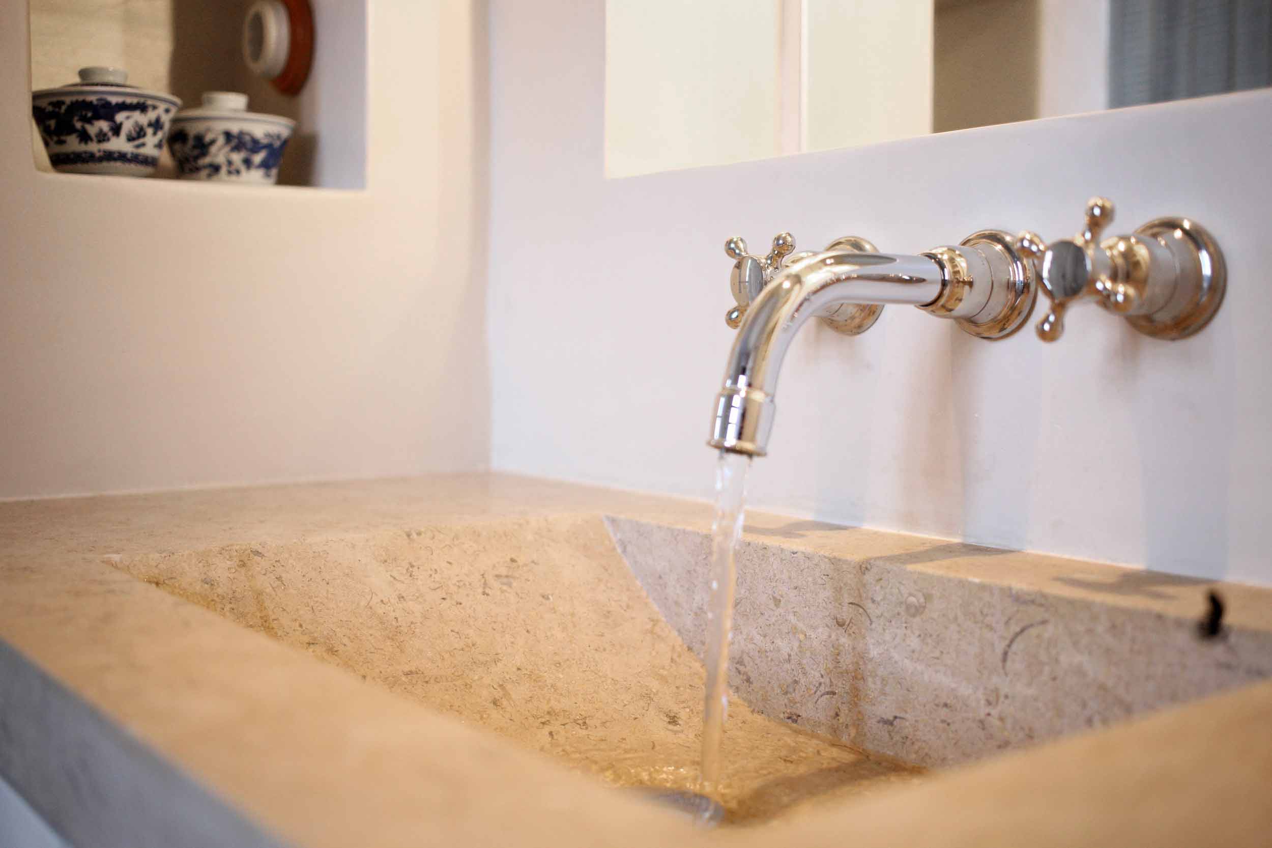 Detalle del lavabo de piedra tallada con grifo cromado de pared y cuencos azules y blancos