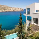 Reforma Cala Carbó con fachada blanca, muro de piedra, jardín y piscina frente a la cala
