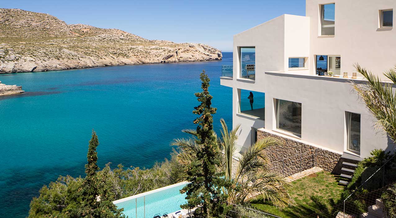 Reforma Cala Carbó con fachada blanca, muro de piedra, jardín y piscina frente a la cala