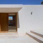 Entrada principal con puerta de madera, muros blancos, muretes de piedra y escalones de piedra clara