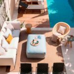 Blick von oben auf die Terrasse mit weißem Sofa, hellblauem Pouf, Teppich, Stühlen und Pool