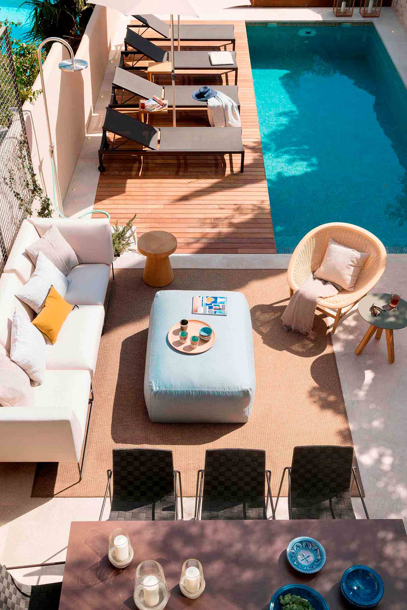 Blick von oben auf die Terrasse mit weißem Sofa, hellblauem Pouf, Teppich, Stühlen und Pool