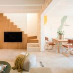 Wohnzimmer mit Holzmöbel, in das Fernseher und Treppe integriert sind, und Esszimmer mit Lederstühlen