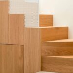 Detail der Treppenstufen aus hellem Holz, mit weißem Lochblechpaneel und Steinstufe