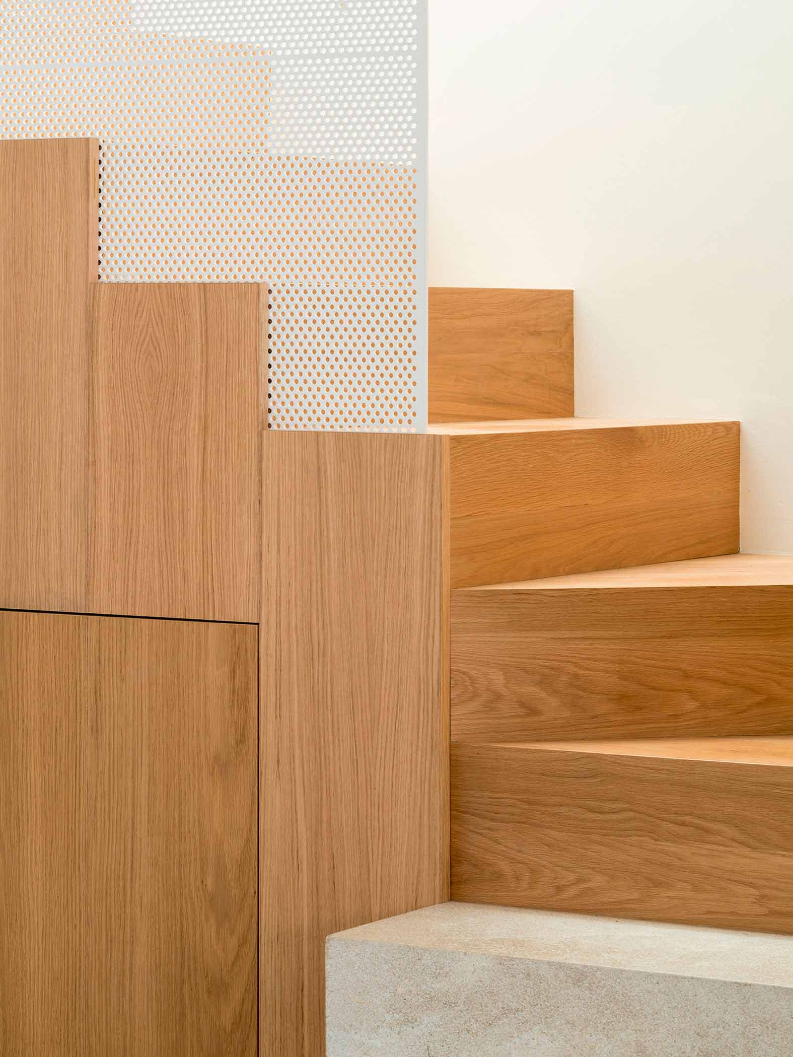 Detail der Treppenstufen aus hellem Holz, mit weißem Lochblechpaneel und Steinstufe