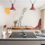Kücheninsel mit Kochfeld und Essbereich im Hintergrund mit Wandbild aus bunten geometrischen Formen