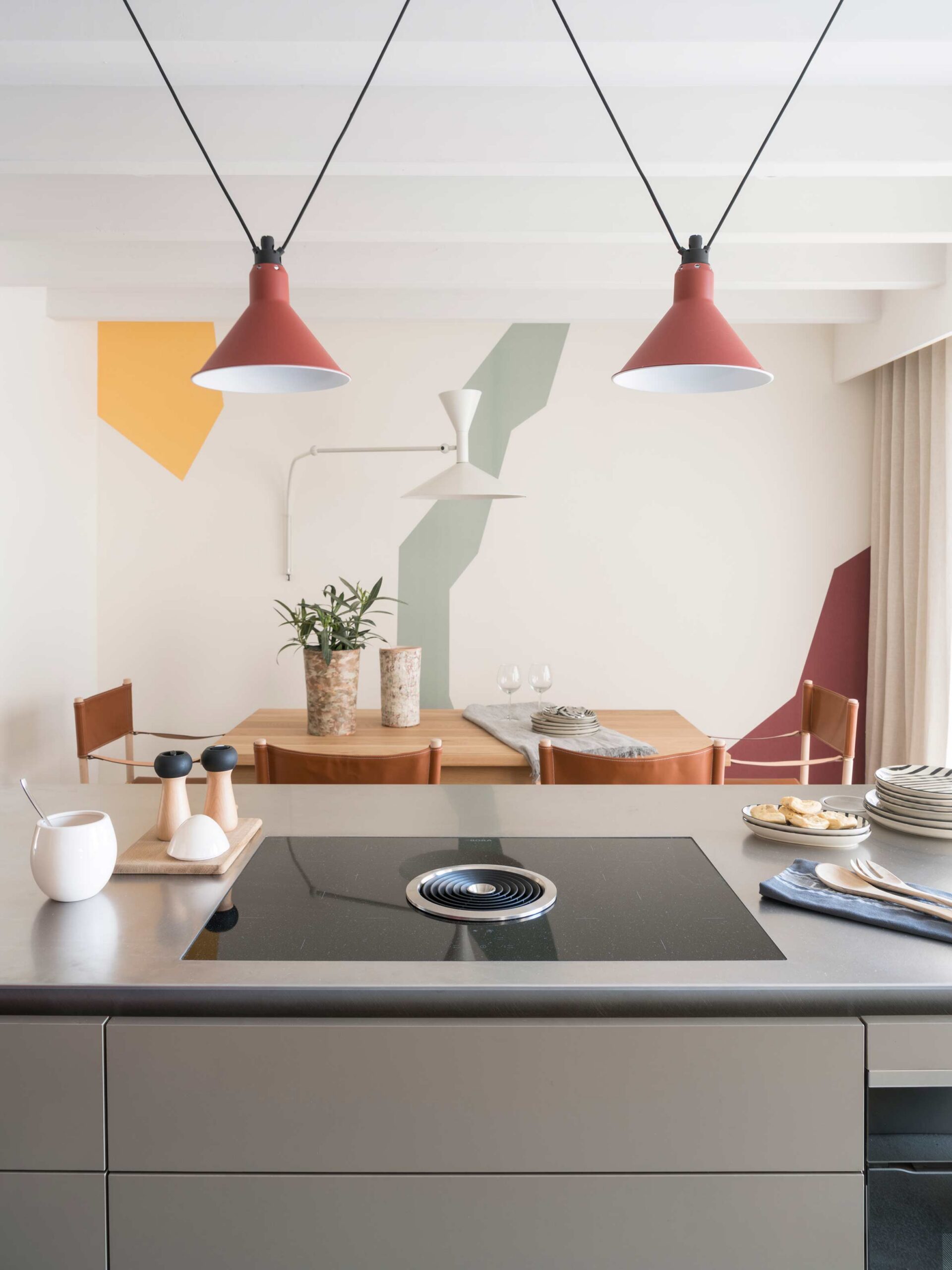 Kücheninsel mit Kochfeld und Essbereich im Hintergrund mit Wandbild aus bunten geometrischen Formen