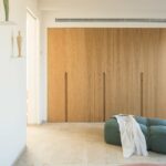 Einbauschrank aus hellem Holz mit integrierten Griffen, grünem Pouf und Teppich in einem hellen Schlafzimmer