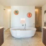 Bad mit weißer freistehender Badewanne vor einer Wand mit beleuchteter Nische und hellem Steinboden